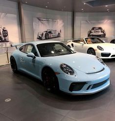 three porsches are on display in a showroom, one is blue and the other is white