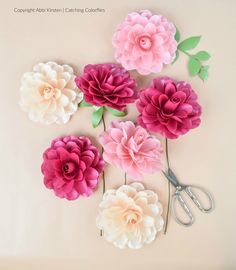 pink and white paper flowers are arranged on the wall next to pair of scissor scissors