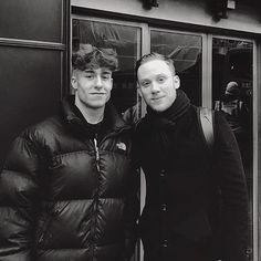 two men standing next to each other in front of a building