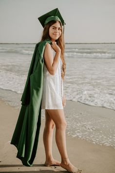 a woman in a graduation cap and gown standing on the beach