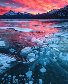 the sun is setting over an icy lake with ice floes and mountains in the background