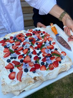 a cake with strawberries and blueberries on it is being cut by two people