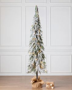 a small christmas tree with presents under it on a wooden floor in front of a white wall