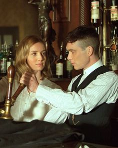 a man and woman standing next to each other in front of a bar with liquor bottles