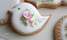 decorated cookies with flowers and leaves are on a white tablecloth, next to some cookies in the shape of birds