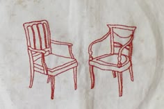 two red chairs sitting next to each other on top of a white cloth covered table