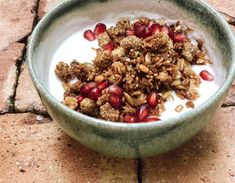 a bowl filled with granola and pomegranate on top of a tile floor