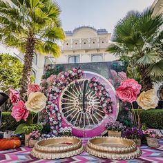 a large clock surrounded by flowers and palm trees