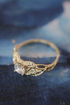 a gold ring with leaves and a diamond in it sitting on a blue cloth covered surface