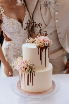 a bride and groom standing next to a wedding cake with chocolate drips on it