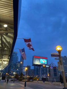 the canadian flag is flying at night in front of some tall buildings with lights on them