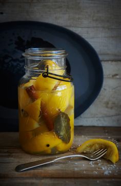 a glass jar filled with sliced fruit next to a knife and fork on top of a wooden table