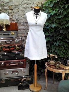 a mannequin dressed in white stands next to several suitcases and a table