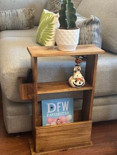 a small wooden shelf with books on it next to a couch and potted plant