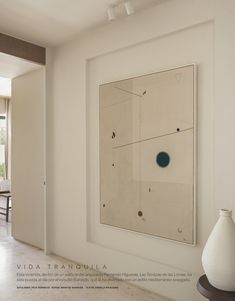 a white vase sitting in front of a painting on the wall next to a table