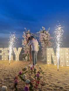 a woman standing on top of a sandy beach next to flowers and sparklers in the sky