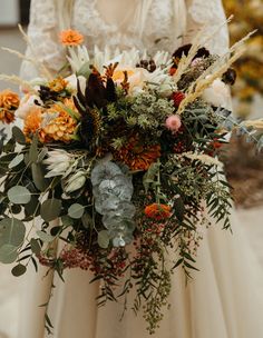 a bride holding a bouquet of flowers and greenery on her wedding day in front of the camera