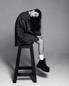 a woman sitting on top of a wooden stool next to a black and white photo