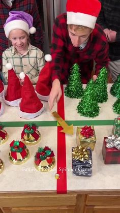 children in santa hats are decorating small christmas trees and presents on a counter top