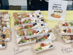 several trays of different types of food on a table with a sign in the background