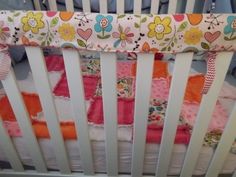 a baby crib with pink and orange quilts on it