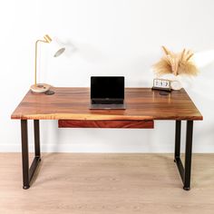 a laptop computer sitting on top of a wooden desk next to a lamp and plant