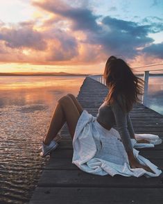 a woman is sitting on a dock by the water