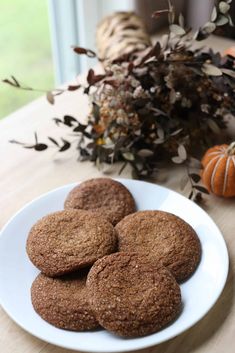 four cookies on a white plate next to a vase with leaves and pumpkins in the background