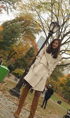 a woman is standing on the street with her hand in her hair and holding onto a lamp post