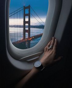 a woman's hand is on the window of an airplane looking out at the golden gate bridge