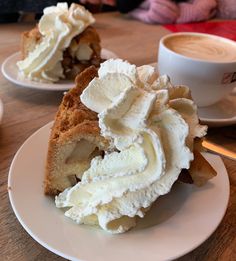 a piece of cake on a plate with whipped cream around it and a cup of coffee in the background