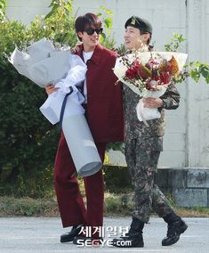 two young men walking down the street with flowers in their hands and one holding a bouquet