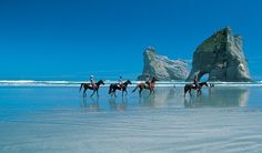 four people riding horses on the beach near an arch in the sand and rock formations