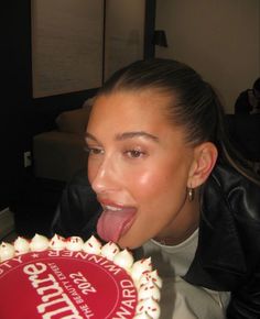 a woman sticking her tongue out while holding a cake with white frosting on it