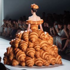 a woman in a dress made out of croissants is walking down the runway