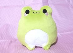 a green stuffed animal sitting on top of a pink blanket with eyes wide open and one eye closed