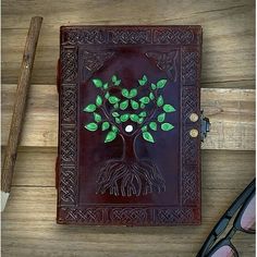 a leather book with a tree on the cover and glasses next to it, sitting on a wooden table