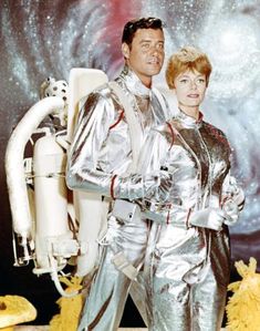 a man and woman dressed in silver standing next to each other near a space station