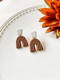 a pair of brown and white earrings sitting on top of a plate next to a flower