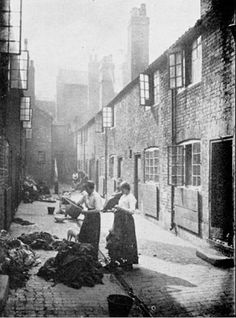 an old black and white photo of two women standing in the alleyway between buildings