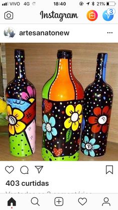 three colorful painted bottles sitting on top of a wooden table next to a vase filled with flowers