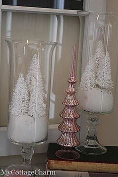 two glass vases with snow on them sitting next to each other in front of a window