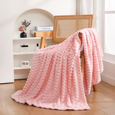 a pink blanket sitting on top of a wooden chair next to a white shelf and window