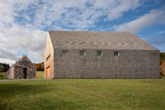 an old brick building sits in the middle of a grassy field with two stone buildings