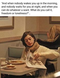 a woman sitting at a table reading a newspaper with another person in the background eating food