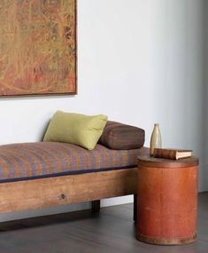 a wooden bed sitting next to a table with a bottle on it and a painting hanging above