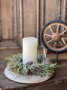 a white candle sitting on top of a wooden table next to a wheel and pine cones