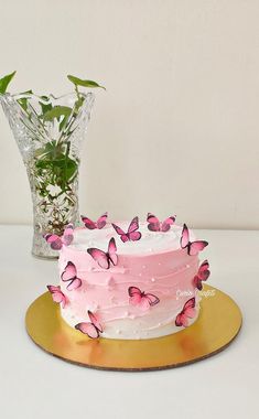 a cake with pink frosting and butterflies on it next to a vase filled with flowers