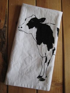 a black and white cow on a white towel sitting on top of a wooden floor