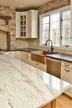 a large kitchen with white cabinets and marble counter tops in front of a brick wall